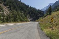 a man riding on a motorcycle down the middle of the road next to a mountain