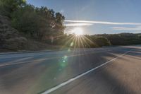 a motorcyclist with a helmet is on the road, passing the sun