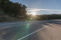 a motorcyclist with a helmet is on the road, passing the sun