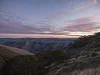 a view over some hills in the sun set with a pink sky overhead in this photograph