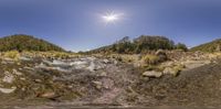 a creek with some rocks and water with sun in the background and the blue sky