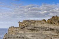 a man sitting on top of a mountain near rocks and clouds over the ocean and a dog looking at it