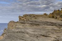 a man sitting on top of a mountain near rocks and clouds over the ocean and a dog looking at it