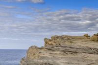 a man sitting on top of a mountain near rocks and clouds over the ocean and a dog looking at it