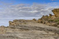 a man sitting on top of a mountain near rocks and clouds over the ocean and a dog looking at it