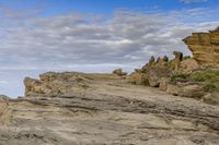 a man sitting on top of a mountain near rocks and clouds over the ocean and a dog looking at it