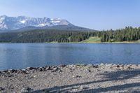 a person with a backpack is walking next to a lake in the wilderness while looking down on a large mountain