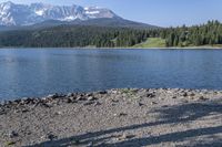 a person with a backpack is walking next to a lake in the wilderness while looking down on a large mountain