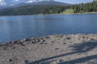 a person with a backpack is walking next to a lake in the wilderness while looking down on a large mountain