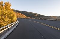 an empty asphalt roadway with a yellow line on the side and mountains in the back