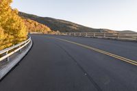 an empty asphalt roadway with a yellow line on the side and mountains in the back