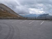 a parked truck sits beside a mountain and lake below clouds in a parking lot on a cloudy day