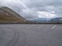 a parked truck sits beside a mountain and lake below clouds in a parking lot on a cloudy day