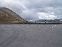 a parked truck sits beside a mountain and lake below clouds in a parking lot on a cloudy day