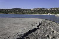 an old, cracky roadway next to the edge of a lake near hills and rocks