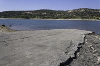 an old, cracky roadway next to the edge of a lake near hills and rocks