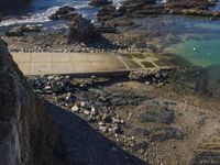 a pier sitting along the side of the ocean with people walking around it surrounded by rocks and boulders