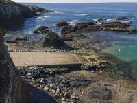 a pier sitting along the side of the ocean with people walking around it surrounded by rocks and boulders