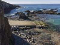 a pier sitting along the side of the ocean with people walking around it surrounded by rocks and boulders