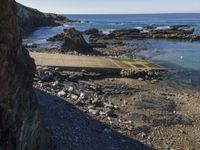 a pier sitting along the side of the ocean with people walking around it surrounded by rocks and boulders