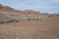 a person is standing near a rock in the desert wearing an orange jacket and blue jeans