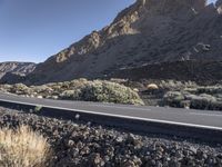 a man on a motor bike is riding down a paved road in the desert near a mountain