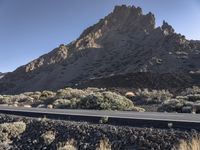 a man on a motor bike is riding down a paved road in the desert near a mountain