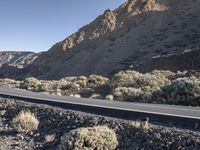 a man on a motor bike is riding down a paved road in the desert near a mountain