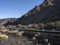 a man on a motor bike is riding down a paved road in the desert near a mountain