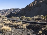 a man on a motor bike is riding down a paved road in the desert near a mountain