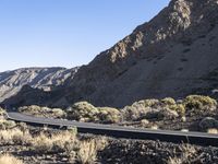 a man on a motor bike is riding down a paved road in the desert near a mountain