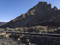 a man on a motor bike is riding down a paved road in the desert near a mountain