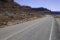 a long and narrow road going through a rocky landscape under a blue sky in the desert