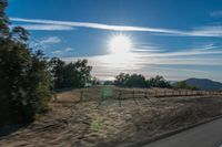 a sun shines brightly behind a wire fence in this photo from inside a car