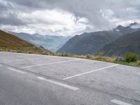 parking lot with mountains in background on hillside near roadway with car parked on road and cloudy skies