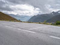 parking lot with mountains in background on hillside near roadway with car parked on road and cloudy skies