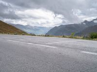 parking lot with mountains in background on hillside near roadway with car parked on road and cloudy skies