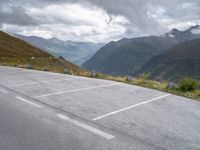 parking lot with mountains in background on hillside near roadway with car parked on road and cloudy skies