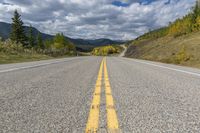 a lone highway with a yellow double - line on it's middle level on a mountain trail in the far distance