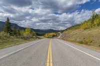 a lone highway with a yellow double - line on it's middle level on a mountain trail in the far distance