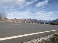 the mountains are near the empty empty road in the middle of the photo and smoke is flying in the air