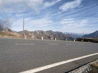 the mountains are near the empty empty road in the middle of the photo and smoke is flying in the air