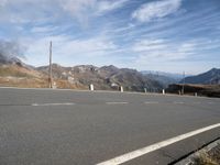 the mountains are near the empty empty road in the middle of the photo and smoke is flying in the air