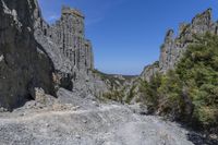 a lone path through a canyon with rock formations in the background with green and blue sky