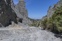 a lone path through a canyon with rock formations in the background with green and blue sky