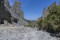 a lone path through a canyon with rock formations in the background with green and blue sky