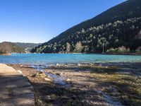 the blue lake is empty near the mountain tops and rocks in front of it and trees on the hill