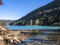 the blue lake is empty near the mountain tops and rocks in front of it and trees on the hill