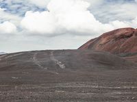 a person is standing near some mountains on a dirt road holding their umbrella and carrying something