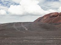 a person is standing near some mountains on a dirt road holding their umbrella and carrying something